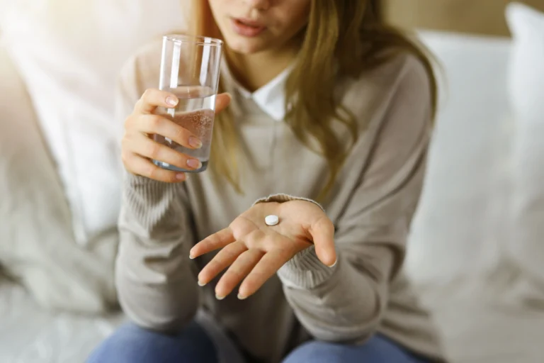 Mulher segurando copo de água e comprimido em tratamento domiciliar de câncer de pele com o medicamento Vismodegibe pelo plano de saúde.