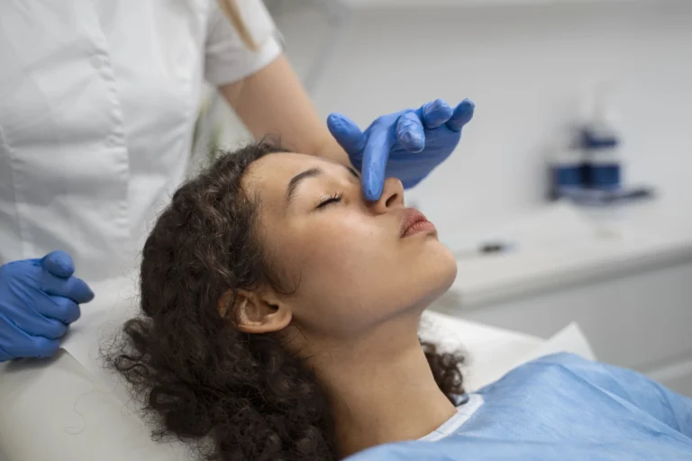 Foto realista de uma paciente deitada em uma maca de clínica médica, com os olhos fechados, passando por uma avaliação ou procedimento no nariz com um profissional de saúde de luvas azuis, representando os cuidados e a preparação necessários antes de realizar uma cirurgia de septoplastia pelo plano de saúde.
