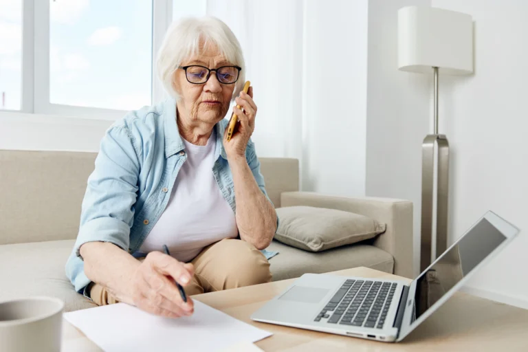 Idosa em ambiente residencial organizando documentos de laudos clínicos e fazendo contato telefônico para reverter conduta abusiva de auditoria do plano de saúde que exige segunda opinião médica.
